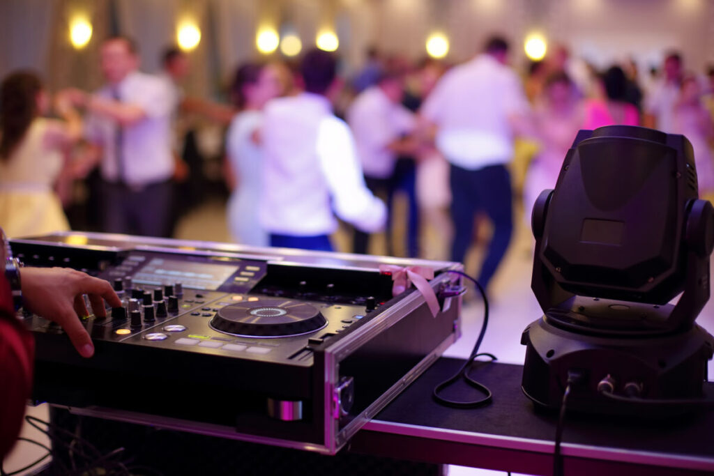 DJ playing music at a wedding, guests dancing in the background