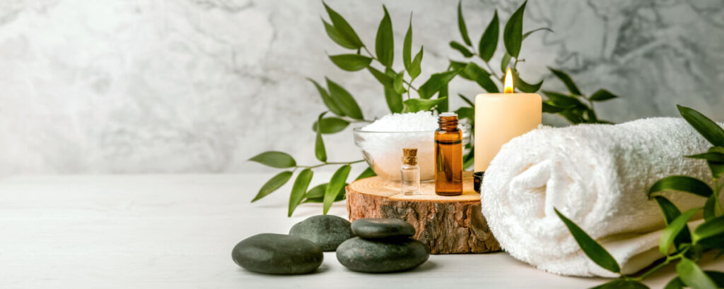 spa products including a towel, essential oils, salt, hot stones, a candle, and some eucalyptus plant