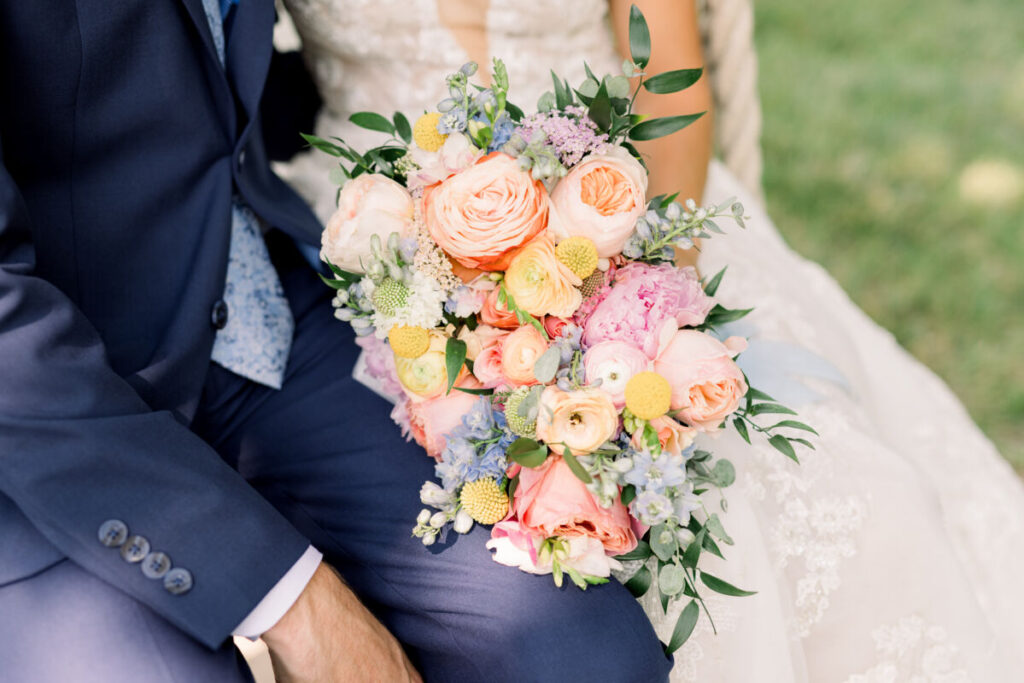 bride holding her flower bouquet sitting next to the groom, close up on the colorful pastel flowers