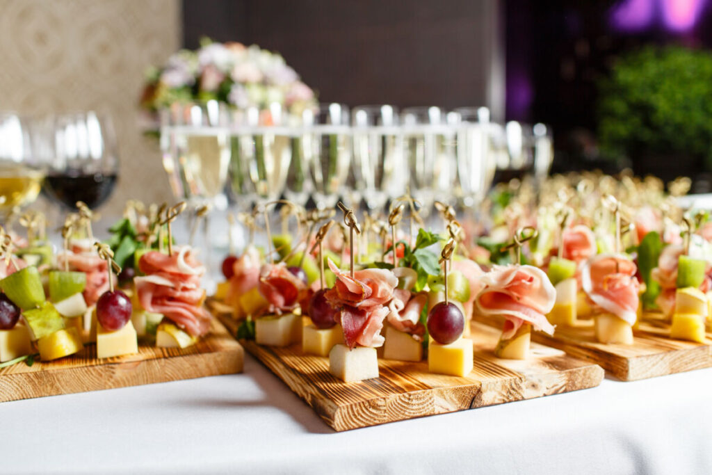 an assortment of appetizers at a wedding including meat and cheese skewers with glasses of champagne and wine in the background