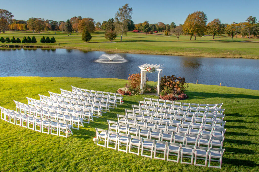outdoor wedding venue overlooking a country club with a lake, fountain, ceremony arch and chairs