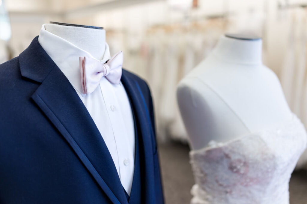 a mannequin of a groom's suit with a pink bowtie, next to a mannequin of a white strapless wedding dress