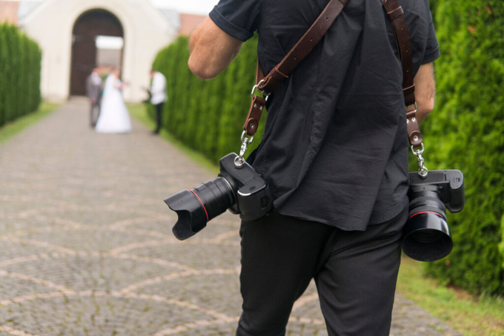 wedding photographer walking towards the bride and groom outside with his cameras