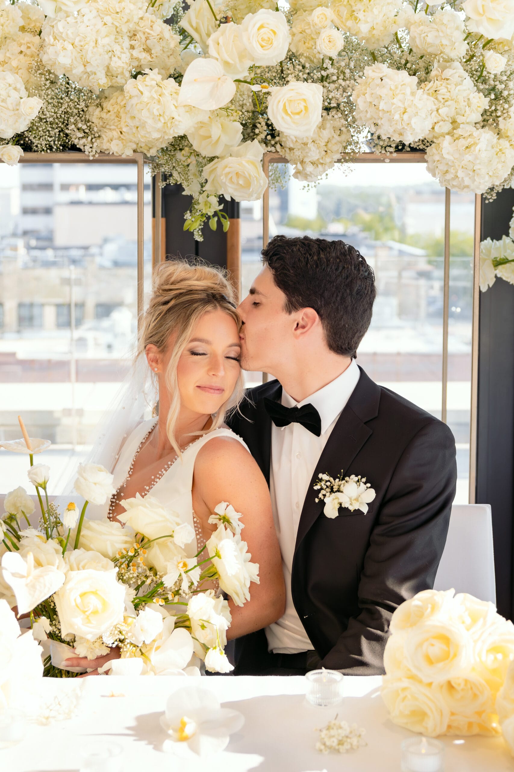 man kissing brides cheek under flower arch scaled
